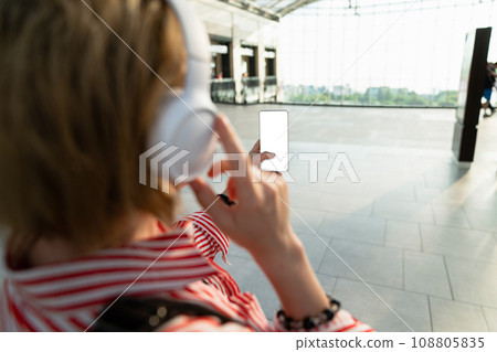 Woman listening to music on headphones and holding a mobile phone in a shopping mall 108805835