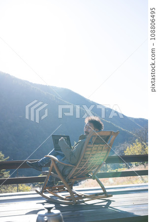 A freelance-looking man working remotely on a wooden deck in the countryside with a view of autumn and winter A freelance-looking man working remotely on a wooden deck in the countryside with a view of autumn and winter 108806495