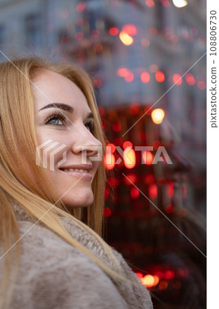 Portrait of a smiling attractive blue-eyed woman against the background of a red store window. Holiday weekend outdoor. Vertical frame 108806730