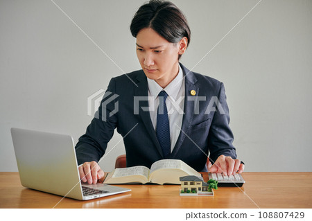 一位男律師一邊看電腦一邊用計算機計算 一位男律師一邊看電腦一邊用計算機計算 108807429