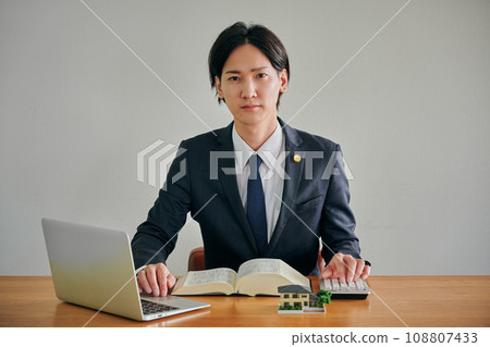 A male lawyer calculates on a calculator while looking at the Six Laws Complete Book and a computer A male lawyer calculates on a calculator while looking at the Six Laws Complete Book and a computer 108807433
