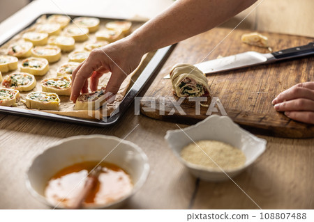 The cook places raw mini puff pastry cookies on a baking sheet. 108807488