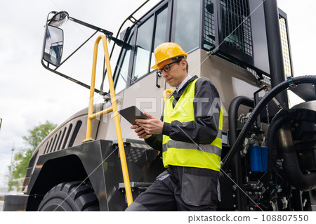 Engineer with tablet computer stands on the stairs to the cab of a truck Engineer with tablet computer stands on the stairs to the cab of a truck 108807550