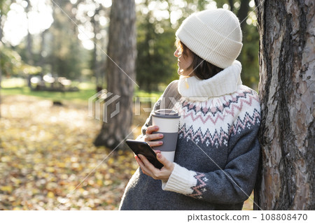 A woman is holding a phone and a cup of hot drink A woman is holding a phone and a cup of hot drink 108808470