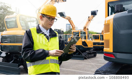 Engineer in a helmet with a digital tablet stands next to construction excavators. 108808493