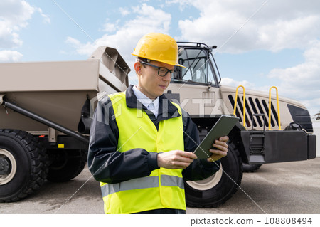 Man worker with tablet computer stands next to mining truck. Man worker with tablet computer stands next to mining truck. 108808494