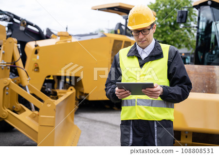 Engineer with digital tablet next to road construction machine 108808531