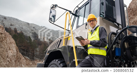 Engineer with tablet computer stands on the stairs to the cab of a truck Engineer with tablet computer stands on the stairs to the cab of a truck 108808532