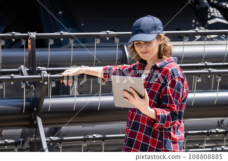 Woman farmer with digital tablet on a background of harvester. Woman farmer with digital tablet on a background of harvester. 108808885