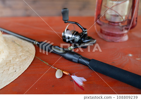 Close-up of spinning rod, straw hat, lantern and mug on wooden table Close-up of spinning rod, straw hat, lantern and mug on wooden table 108809239