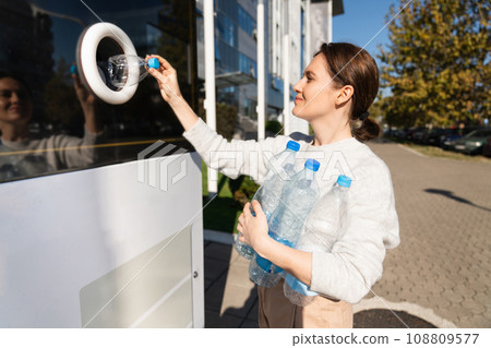 Woman uses a self service machine to receive used plastic bottles and cans on a city street 108809577