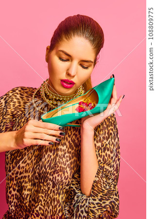 Portrait of lady dressed animal print blouse holding heel full of capsules, vitamins, pills, medications over pink background 108809775