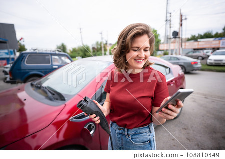 Woman charging red electric car. 108810349