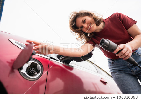 Woman charging red electric car. 108810368