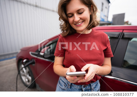 Woman charging red electric car. 108810377