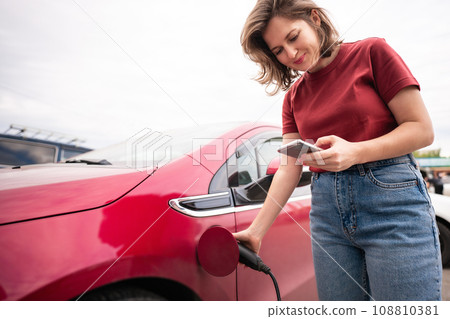 Woman charging red electric car. 108810381