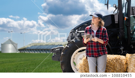 Woman farmer with a digital tablet and agricultural tractor 108810455