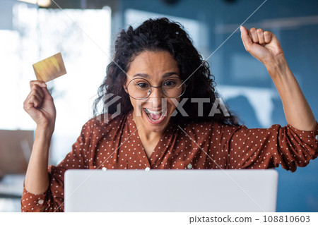 Happy joyful woman bought bargain online product with discount, business woman celebrating successful online shopping at workplace inside office, holding bank credit card, using laptop. 108810603