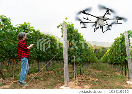 Woman farmer controls drone sprayer with a tablet. 108810915