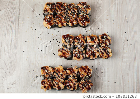 Set of baked sushi rolls sprinkled with sesame seeds on a white wooden background. 108811268