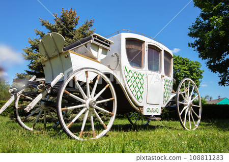 An antique white carriage from the nineteenth century on a green lawn. The prototype of a modern car. 108811283