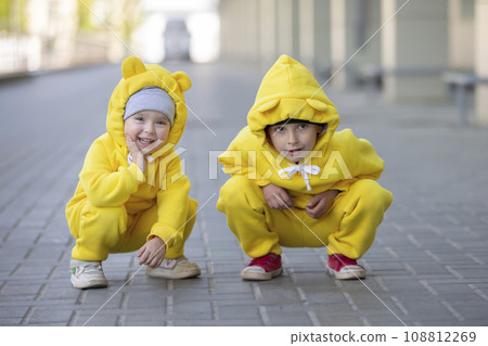 Little brother and sister. Funny children boy and girl in yellow identical suits play outdoors. 108812269