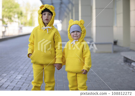 Little brother and sister. Funny kids boy and girl in yellow suits posing, looking at the camera. 108812272