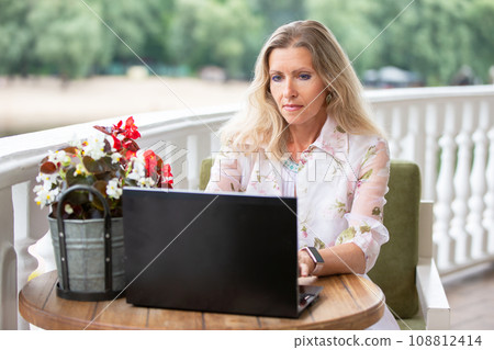 Mature woman in a summer cafe with a laptop. Remote work, freelance. 108812414