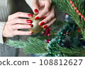 Female hands with red manicure and gold foil on the nails. Winter and Christmas time concept. Manicured woman's hands with Christmas decoration. 108812627