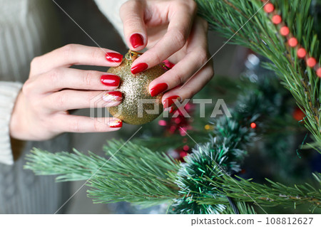 Female hands with red manicure and gold foil on the nails. Winter and Christmas time concept. Manicured woman's hands with Christmas decoration. 108812627