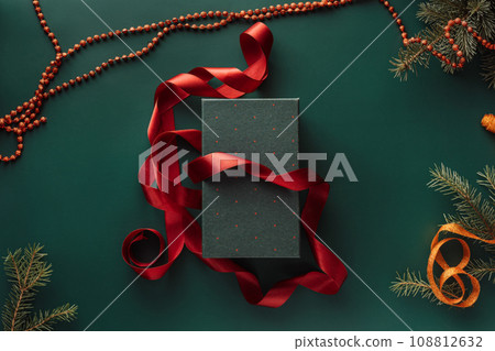 Gift in green packaging and red ribbon on a green background with a Christmas tree 108812632