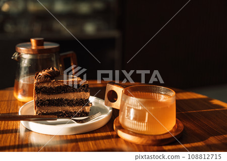 A pistachio piece cut from a cake on a white plate on a wooden table with tea under the sunlight A pistachio piece cut from a cake on a white plate on a wooden table with tea under the sunlight 108812715