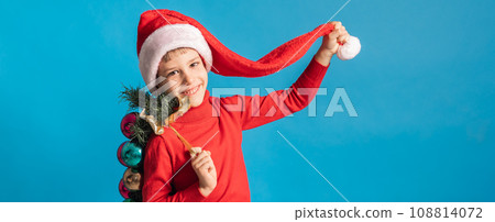 Banner cheerful child in santa hat hold christmas decorative balls on blue background, Xmas and holidays concept mockup. Generation alpha and gen alpha children. 108814072