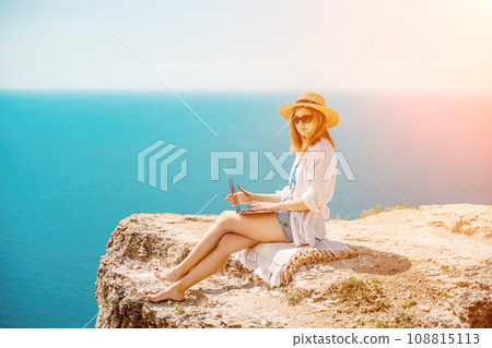 Freelance woman working on a laptop by the sea, typing away on the keyboard while enjoying the beautiful view, highlighting the idea of remote work. 108815113