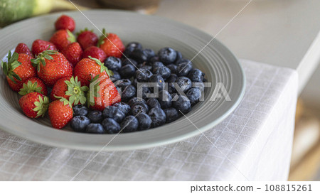 Fresh strawberries and blueberries on a white plate on kitchens table, close-up, selective focus. 108815261