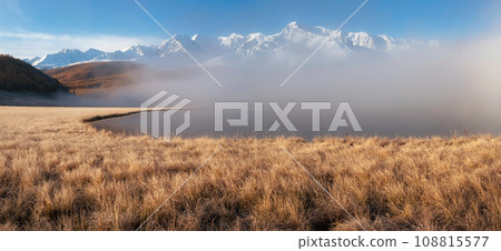 Beautiful sunny foggy morning in the mountains. Autumn frost on dry grass. Snowy peaks. North Chuysky Range and Lake Dzhangyskol. Russia, Altai Republic. Panoramic view. Beautiful sunny foggy morning in the mountains. Autumn frost on dry grass. Snowy peaks. North Chuysky Range and Lake Dzhangyskol. Russia, Altai Republic. Panoramic view. 108815577