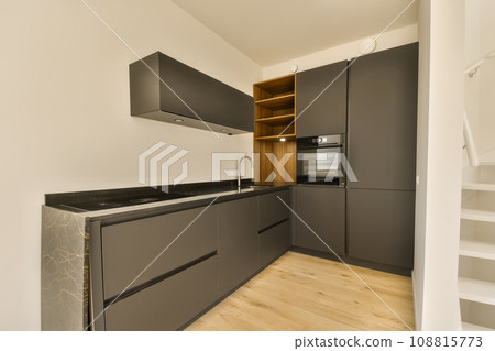 a modern kitchen with wood flooring and black cabinetd cupboards in the center of the room is a white wall 108815773