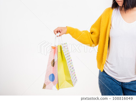 Happy young female hold many packets within arms, woman hand she wears a yellow shirt holding shopping bags multicolor isolated on white background, Black Friday sale concept 108816049
