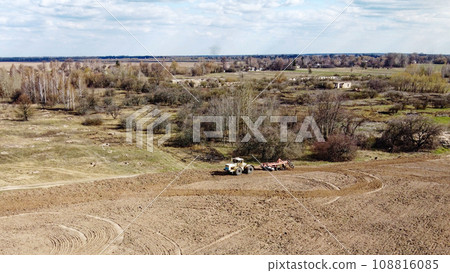 Agricultural machinery in a field near a small grove, aerial view. Agricultural land. Agricultural machinery in a field near a small grove, aerial view. Agricultural land. 108816085
