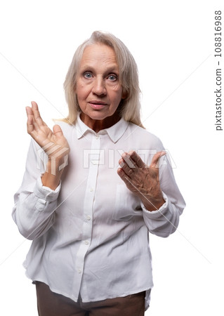 An elderly suspicious woman with gray hair looks carefully at the camera 108816988