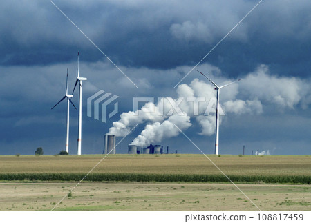 Wind turbines and industrial pipes with smoke on a cloudy day in Germany 108817459