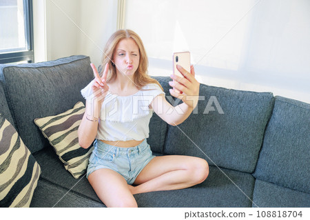 Caucasian girl sitting on the sofa and taking a selfie Caucasian girl sitting on the sofa and taking a selfie 108818704