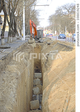 An excavator bucket digs the ground in a trench on the street 108819248