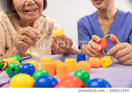 Caregiver and senior woman playing wooden shape puzzles game for dementia prevention 108821304
