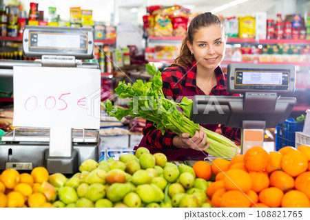 Young saleswoman weighs greens on a scale 108821765