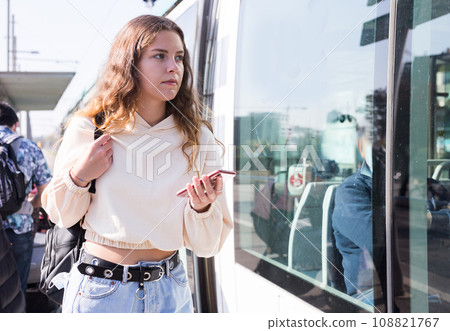 A confident girl with a mobile phone in her hands is about to board a tram 108821767