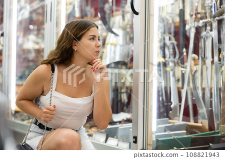 Interested young woman viewing various swords placed on display case 108821943