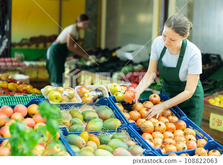 Positive saleswoman laying out pomegranates on display stand in supermarket 108822063