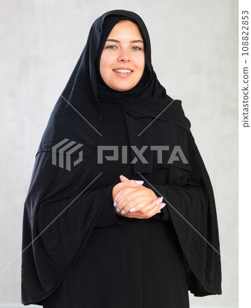 young joyful Muslim woman in traditional hijab clothes poses on gray background. young joyful Muslim woman in traditional hijab clothes poses on gray background. 108822853