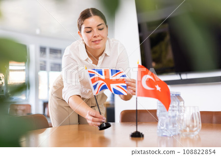 Young female assistant putting up turkish and british flags on table for international negotiations 108822854